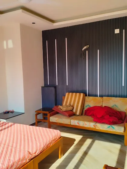 The interior of the Palam Vihar terrace room, featuring a bed and sofa against a modern, vertically paneled accent wall.