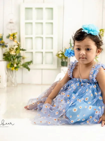 A quiet moment in a field of flowers. This baby girl looks like a little doll in her blue daisy dress during her first birthday studio session.