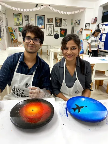 A couple proudly displays their unique resin art creations. One piece is a vibrant galaxy design, while the other features a serene blue sky with an airplane silhouette, showing the endless creative possibilities.