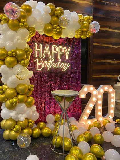 A glamorous 20th birthday setup with a pink sequin wall, a gold and white balloon arch, and '20' marquee numbers.