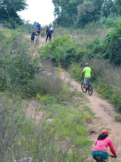 A group cycling down a dirt path in Ramanagara, surrounded by lush greenery.
