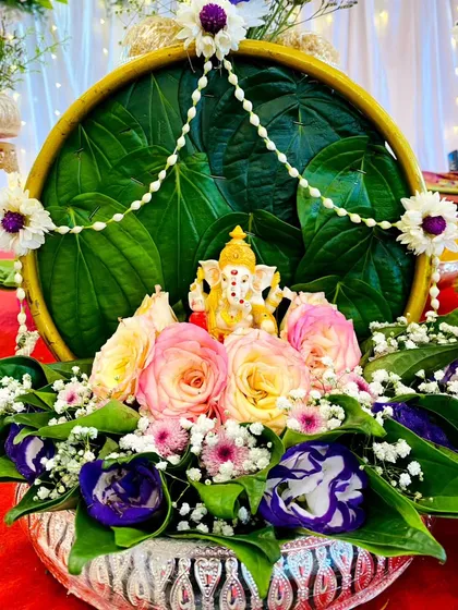 This is a classic Aarthi or welcome tray, featuring a small Ganesha idol for blessings. The arrangement uses fresh betel leaves, vibrant roses, and delicate jasmine garlands, all set in an elegant silver bowl for a traditional ceremony.