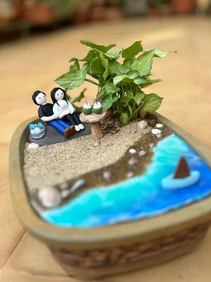 This custom miniature garden is a little world in a planter, telling the story of a couple's relaxing day at the beach.