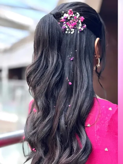 A close-up of the delicate floral arrangement on the half-up ponytail. The tiny flowers scattered through the waves add a whimsical and charming detail.