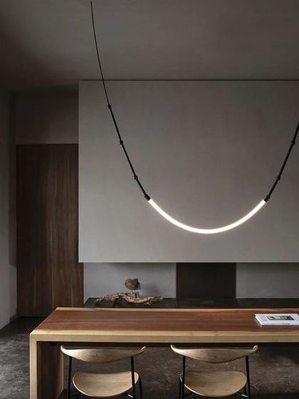 A single, curved Leda pendant hangs over a wooden dining table, its simple form making a powerful minimalist statement.