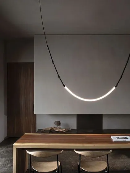 A single, graceful arc of the Leda light over a wooden table. This minimalist configuration highlights the fixture's elegant simplicity and warm, diffused illumination.