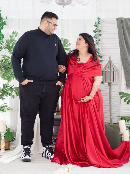 A beautiful couple's portrait in our boho greenhouse set, with the mother-to-be in a stunning red gown.