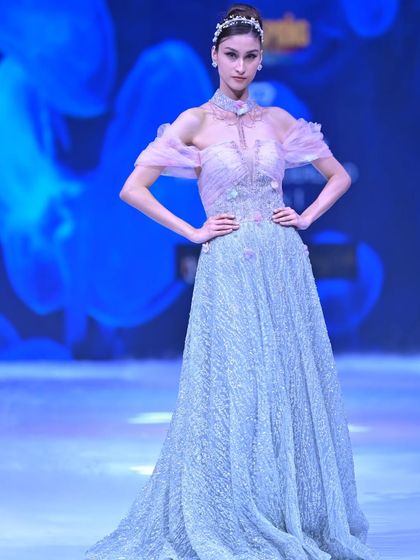 An ethereal creation in ice-blue and pink. This gown features a sparkling, fully embroidered A-line skirt and delicate off-shoulder ruffled sleeves for a touch of romanticism.