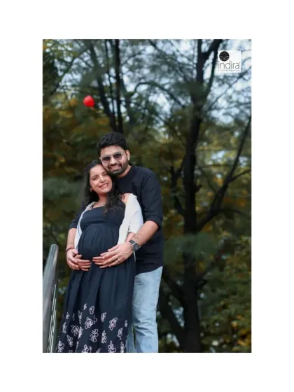 A classic couple's pose during their park maternity shoot, with the father-to-be embracing his partner from behind, both cradling the baby bump.
