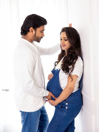 An intimate and loving pose against a simple white wall. The focus is entirely on the couple's connection and their shared anticipation for their new arrival.