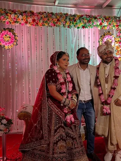 Posing with a happy couple on their wedding day. The stage behind them has a beautiful floral arch with hanging crystal strings.