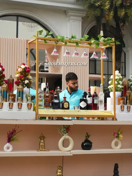 A close-up of the bartender's station at the Banaras-themed event. The decor details, including the hanging glasses and small floral arrangements, are consistent with the overall theme.