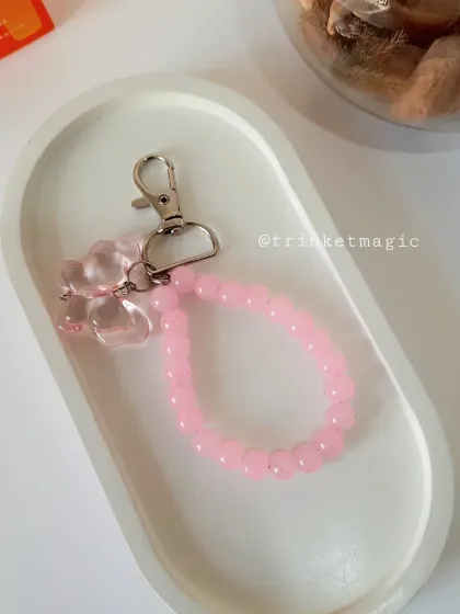 A handmade pink beaded bag charm with a translucent butterfly accent, resting in a decorative tray. A simple way to add a pop of color.