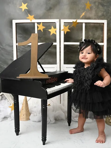 A little musician at her black piano. This dramatic and elegant setup with stars and clouds creates a unique and artistic first birthday portrait.