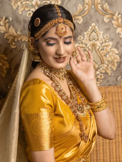 A soft, dreamy portrait of a bride in a mustard yellow silk saree. The makeup features bronze and gold tones on the eyes to match the richness of the saree and jewellery.