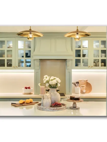 A view into the powder blue kitchen, framed by a doorway. The soft lighting and elegant details, like the custom range hood and glass-fronted cabinets, are perfectly captured, showcasing a dream kitchen.