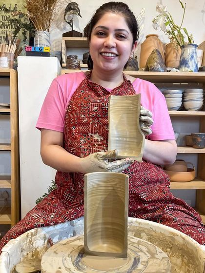 A student proudly displays a cross section of her thrown cylinder, showing the even wall thickness she achieved through dedicated practice.
