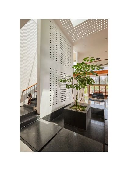 A central planter in the Vikas Residence is surrounded by dark stone flooring, creating a focal point. The perforated wall and skylight above add layers of light and texture.