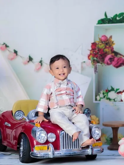 This little boy is all smiles as he sits on top of a red vintage toy car, ready to celebrate his first birthday in style.