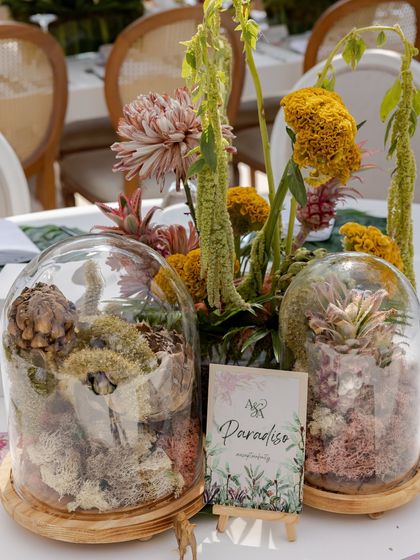 A wedding lunch tablescape where elegance meets romance. The centerpiece features unique florals and fruits in a glass cloche, creating a 'paradise' theme.
