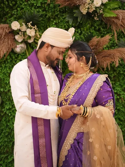 A candid, happy moment between the bride and groom. Her traditional purple saree and gold jewellery are key elements of the Maharashtrian wedding style.