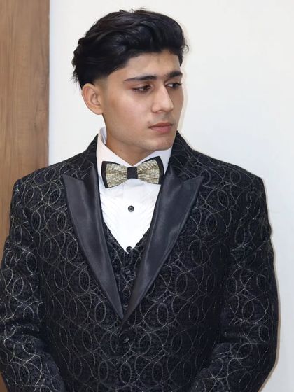 This black three piece suit features a textured fabric with a subtle shimmer, perfect for evening events. The look is completed with a custom waistcoat and a gold-flecked bow tie for that extra touch of class.