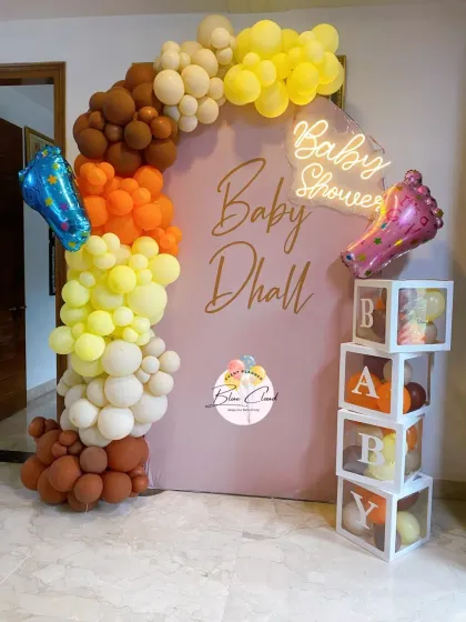A warm-toned 'Baby Dhall' baby shower setup with a custom backdrop, 'BABY' blocks, and an organic balloon garland.