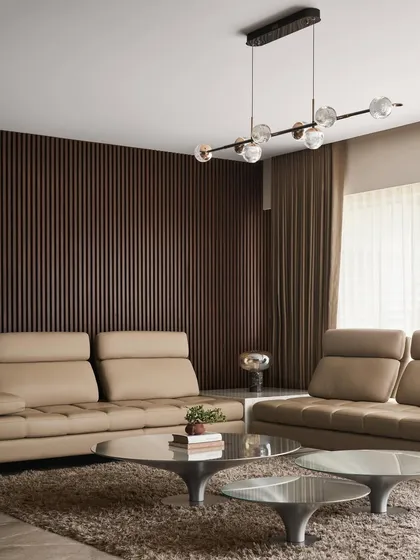 In this living room, I paired plush leather sofas with a fluted wood accent wall. The space is grounded by a set of sculptural metal coffee tables and illuminated by a modern linear chandelier, creating a warm and sophisticated environment.