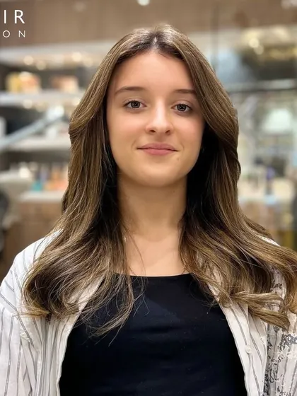 A happy client showing off her new, natural-looking brown hair color. The subtle layers and soft coloring give her a fresh and youthful appearance.