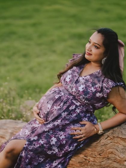 A serene outdoor maternity portrait. The mom-to-be is relaxing on a fallen log in a field of green, creating a calm and natural scene that beautifully highlights her pregnancy glow.