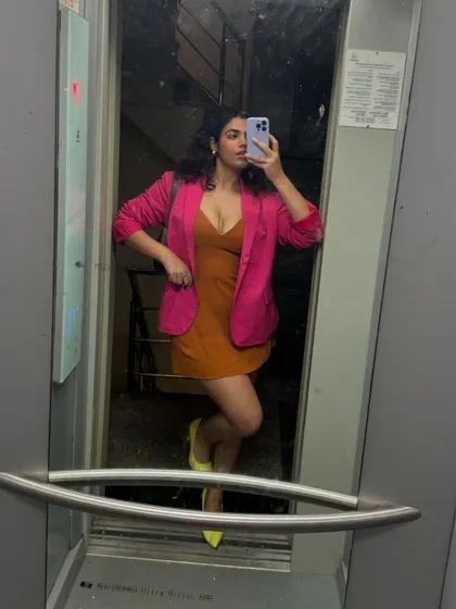 A classic elevator selfie. This look is all about color blocking, with a hot pink blazer over a rust-colored dress and bright yellow heels. It's a bold and confident look for a birthday celebration.