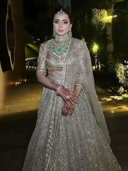 A full-length shot of a bride at her wedding venue. Her hair is in a classic bun, which keeps her look elegant and ensures her jewelry and outfit are the main focus.