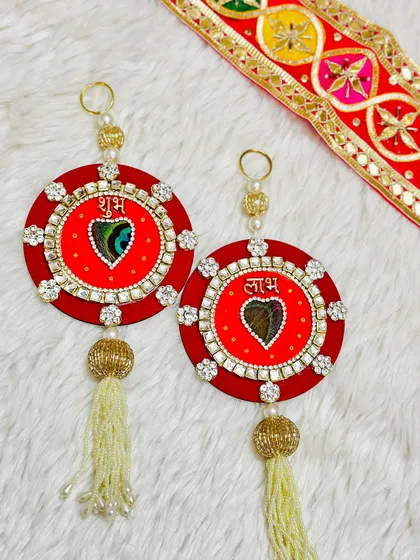 A classic red Shubh Labh hanging set, featuring a peacock feather at the heart of the design. The stone work border adds a touch of sparkle to this auspicious piece.