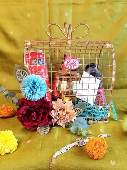 This birdcage-style metal hamper is a unique gift for your bhai and bhabhi. It's filled with a mix of his and her favorites, decorated with flowers, and lit with fairy lights.