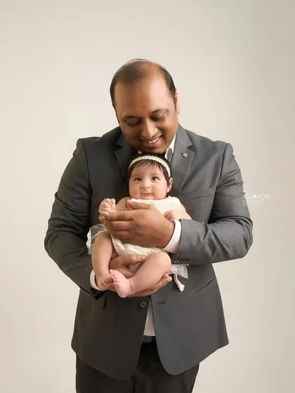 A father looks down at his baby with a gentle smile, his hands securely supporting her. A simple, powerful portrait of paternal love.