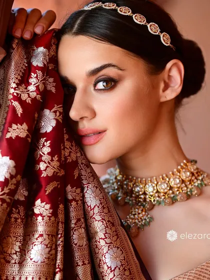 A close-up shot for the brand Elezara, where the rich fabric of the Banarasi saree is the focus. The model's pose draws the viewer's eye to the intricate silver and gold floral patterns of the weave.