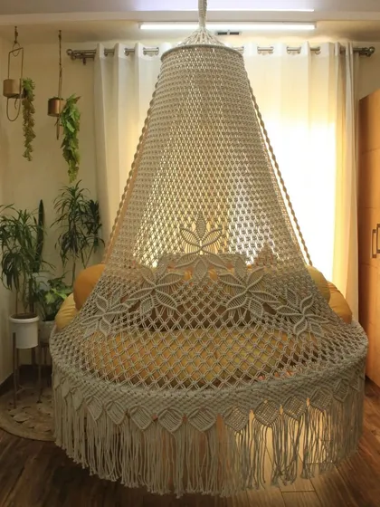 A full view of our bed swing in a natural off-white color. The canopy is covered in a beautiful floral macrame pattern, making it a true statement piece.