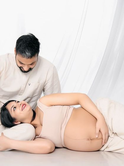 A relaxed and candid moment from a minimalist maternity session. The mom-to-be lies comfortably with her head in her partner's lap, sharing a happy and natural smile.
