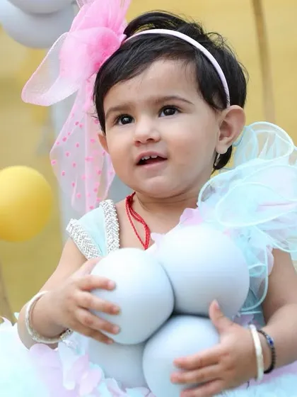 The birthday girl looking up with curiosity while holding a string of balloons. These spontaneous moments are perfect for capturing a child's personality during their birthday shoot.