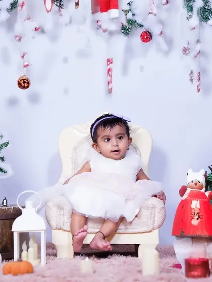 A festive Christmas portrait in the studio. The little girl is dressed in white, surrounded by miniature Christmas trees and decorations, creating a perfect holiday card photo.