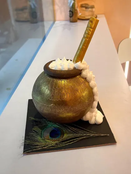 This Krishna-themed piñata cake is a smash hit for celebrations. The exterior is a golden 'matka' (pot) with overflowing butter, and inside holds a sweet surprise. The peacock feather adds a divine touch.