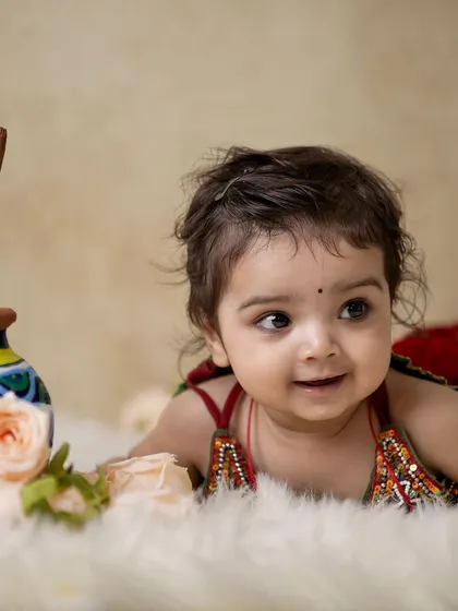 This is a duplicate of image 128. A candid shot of a baby girl in her Radha costume, lying on a soft fur rug.