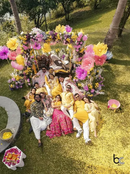 An aerial shot of the entire family relaxing on the grass after a fun and tiring Haldi ceremony, surrounded by colorful floral decor.