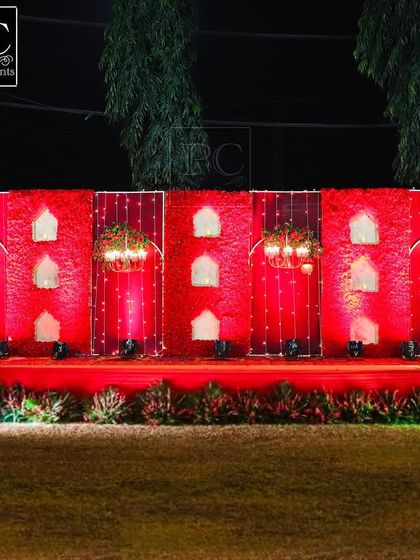 A bold and dramatic wedding stage design. The entire backdrop is a wall of red carnations with traditional 'jharokha' style windows, creating a look of royal Rajasthani architecture.