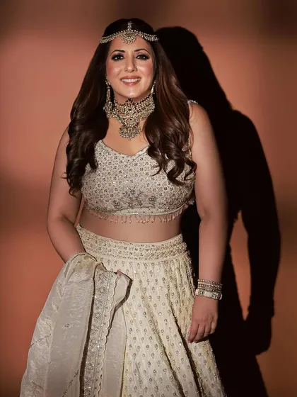 A confident and smiling pose in a stunning ivory lehenga. The styling is traditional yet fresh, perfect for sangeet or reception events.