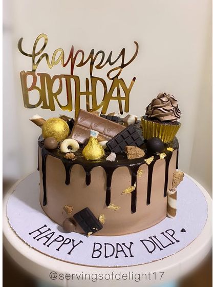 A chocolate lover's dream! This drip cake is loaded with various chocolates, a mini cupcake, and gold accents for a truly decadent birthday treat.