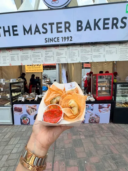 A customer holding a fresh serving of our crispy fried wontons at our outdoor stall. These golden pockets are filled with a savory vegetable mix and served with a tangy dipping sauce, perfect for a quick and satisfying snack.