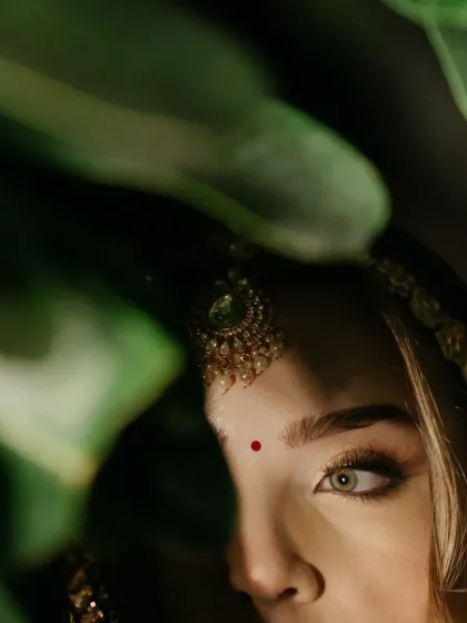 An artistic close-up of the bride's eye, peeking through green leaves. A creative and intriguing bridal portrait.