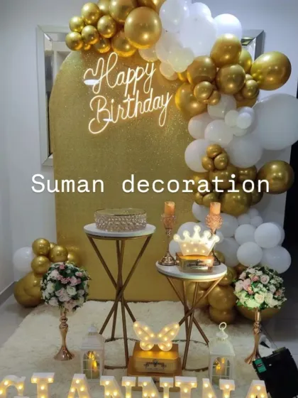 A luxurious white and gold themed birthday party. The decor features a gold glitter backdrop, an elegant balloon garland, and beautiful dessert stands with floral arrangements.