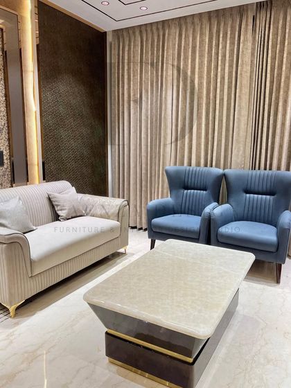 A well-balanced living room featuring a beige channel-tufted sofa, two blue high-back chairs, and a coffee table with a natural onyx top. The space feels both formal and inviting.